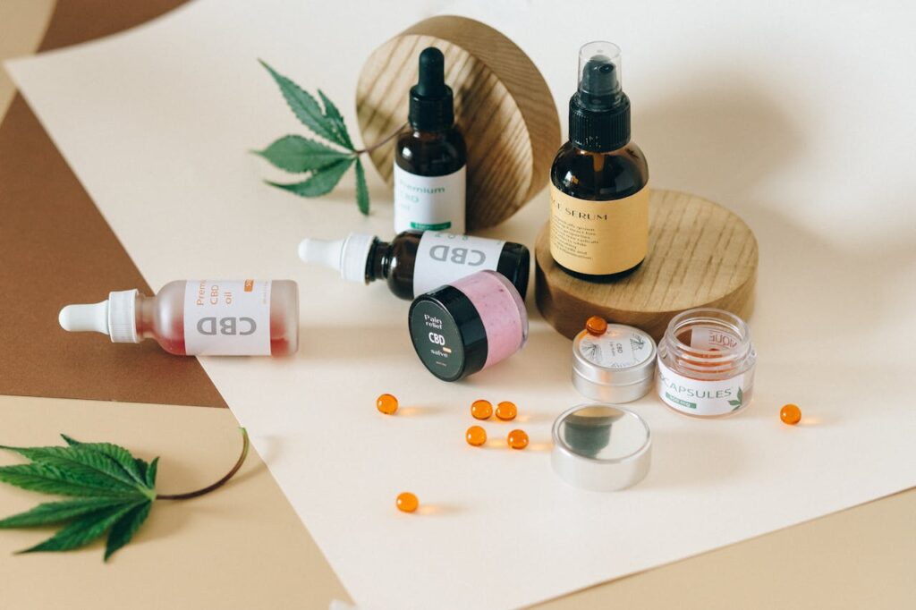 CBD products including oil tinctures, face serum, pain relief salve, capsules, and soft gels arranged on a beige surface with